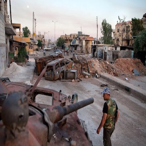 أحد عناصر الجيش السوري الحر يمر بدبابة محترقة تابعة للجيش النظامي شمالَ محافظة حلب، في عام 2012.